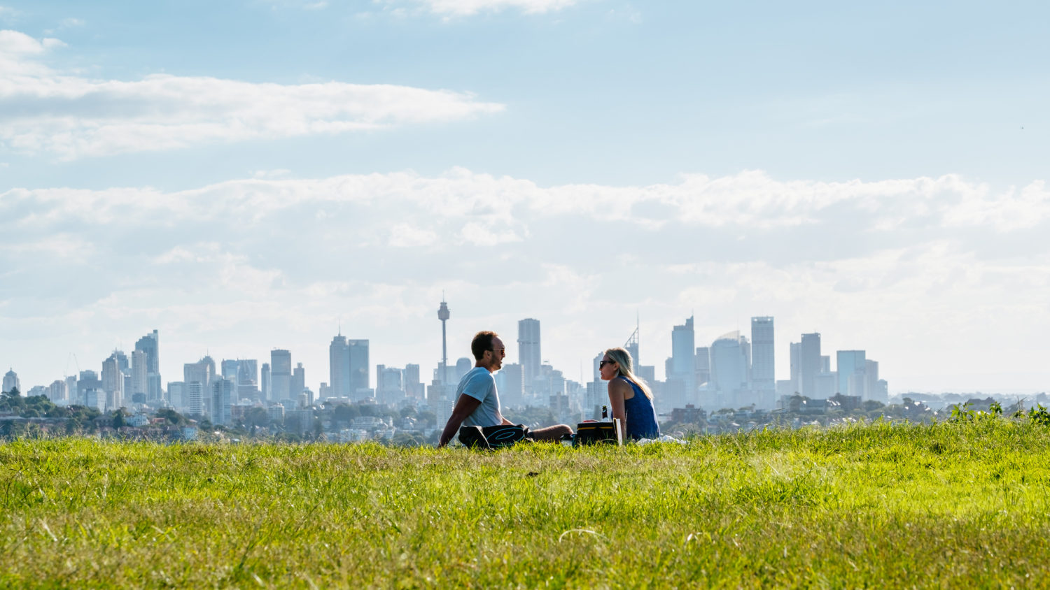 Australia: Couple sitting on field with city skyline in backround