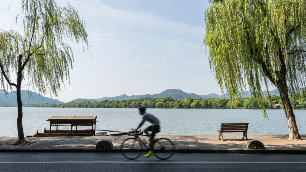 Side view of motion blurred unrecognizable cyclist riding bike against West Lake, Hangzhou, Zhejiang, China